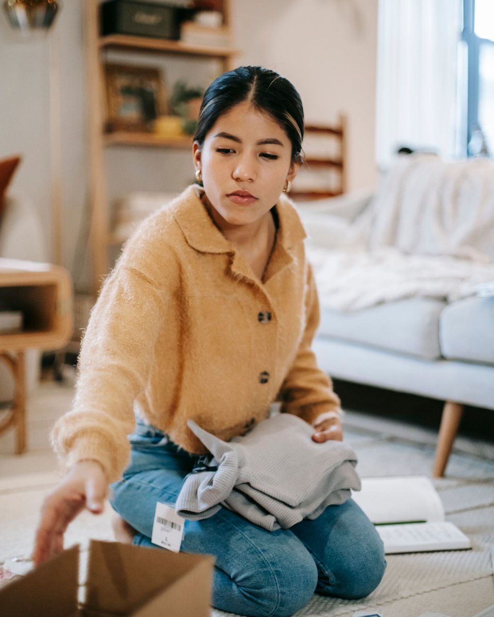 A woman preparing clothes for a cardboard box at home.